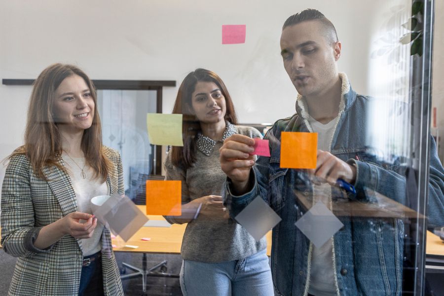 Studierende arbeiten im Team, kleben Aufkleber auf das Glas, machen ein Brainstorming, machen Notizen